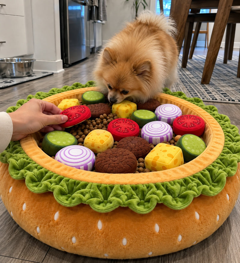 A hand tucking a plush tomato slice into the Burger Burrow while a Pomeranian leans in to watch